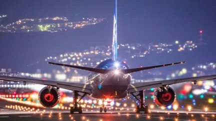 Aircraft taking off at night from a runway illuminated by numerous lights.