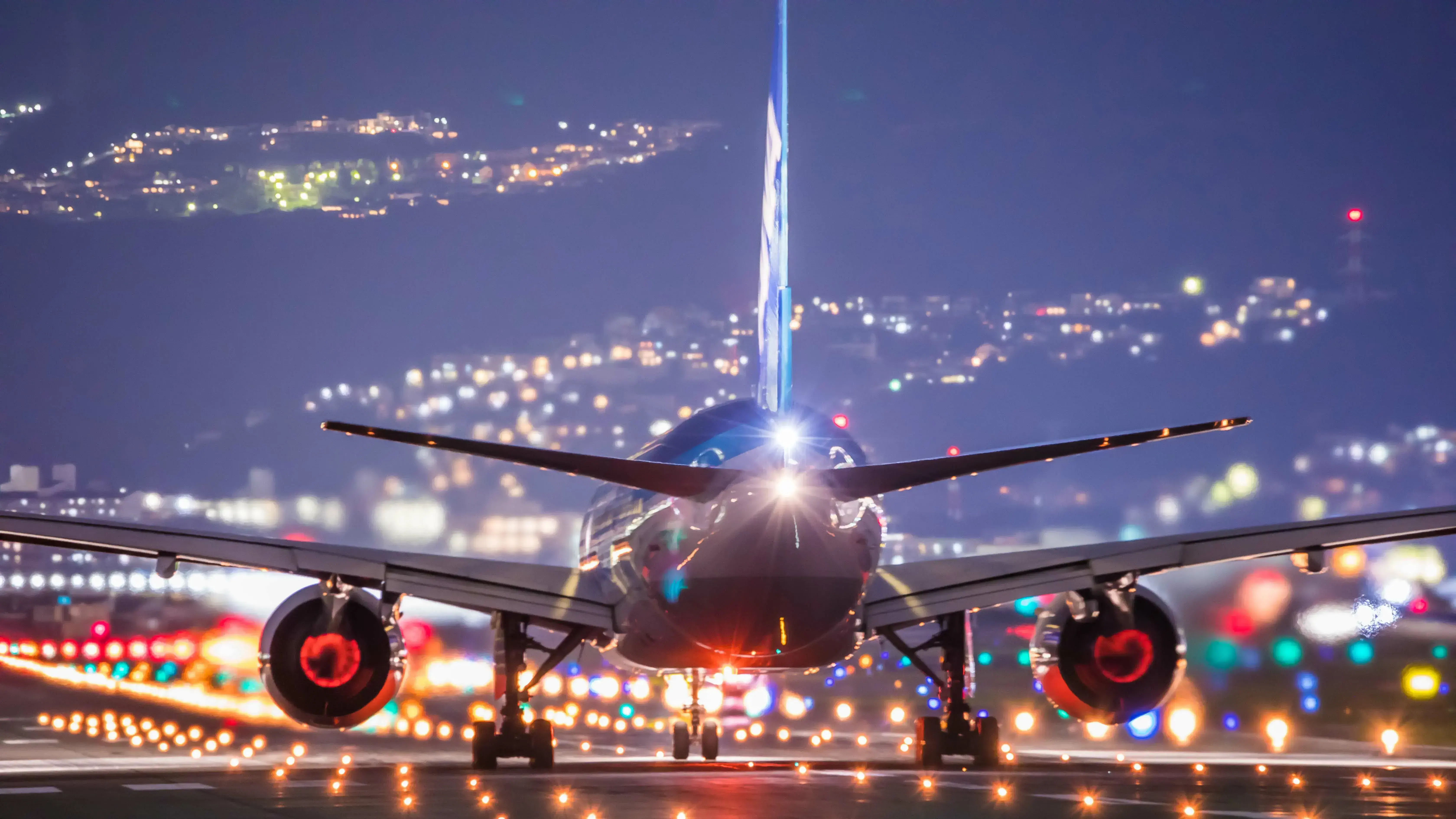 An aircraft on a runway, shown from behind against coloured lights, ready for takeoff